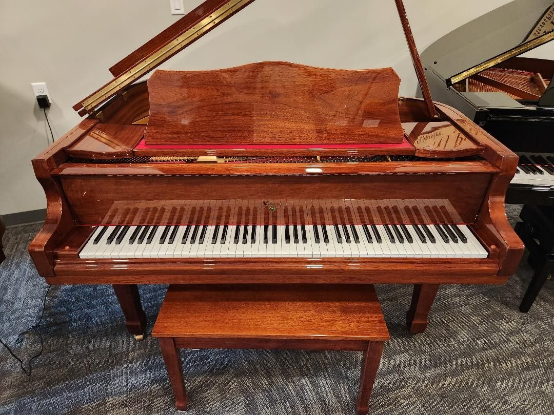 Brown grand piano with bench, open lid, and visible keyboard in a showroom or room