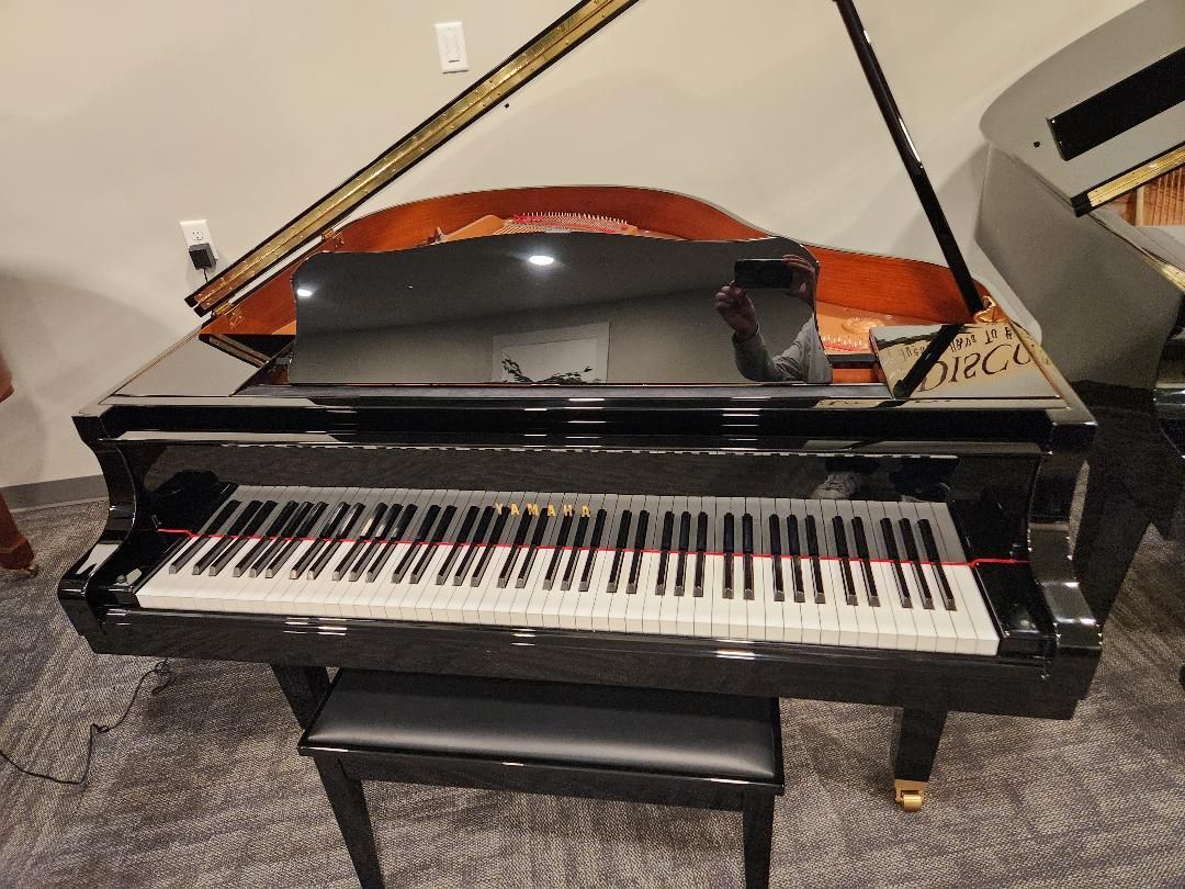 Black grand piano with open lid and bench in a room
