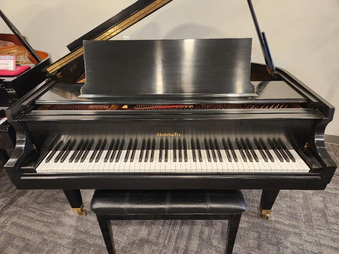 Black grand piano with matching bench, viewed from the front indoors.