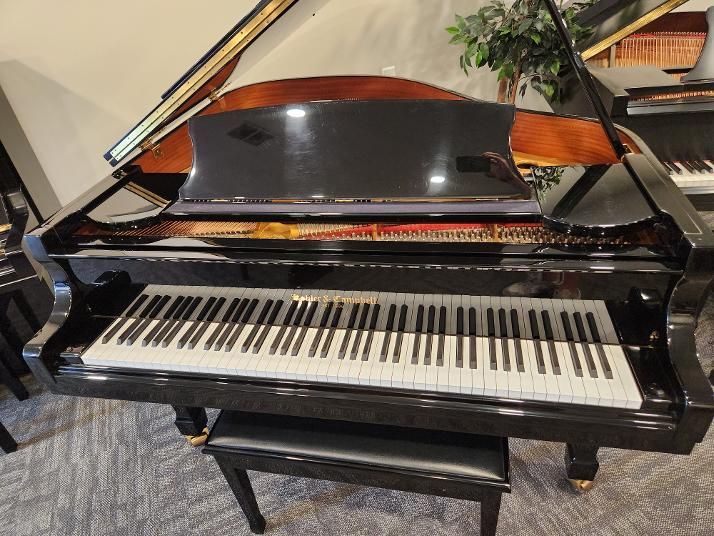 Black grand piano with lid open, viewed from the front in a bright room