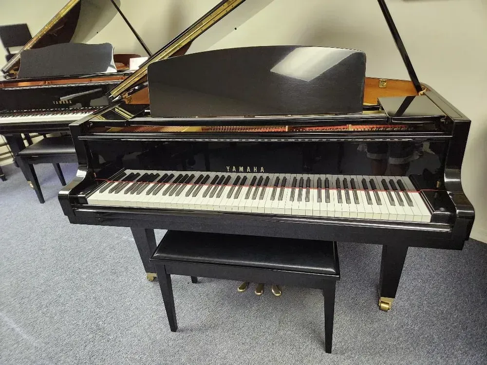 A black grand piano sits in a room with other pianos