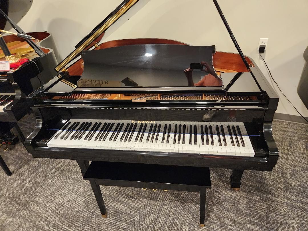 Black grand piano with open lid and bench on a carpeted floor.