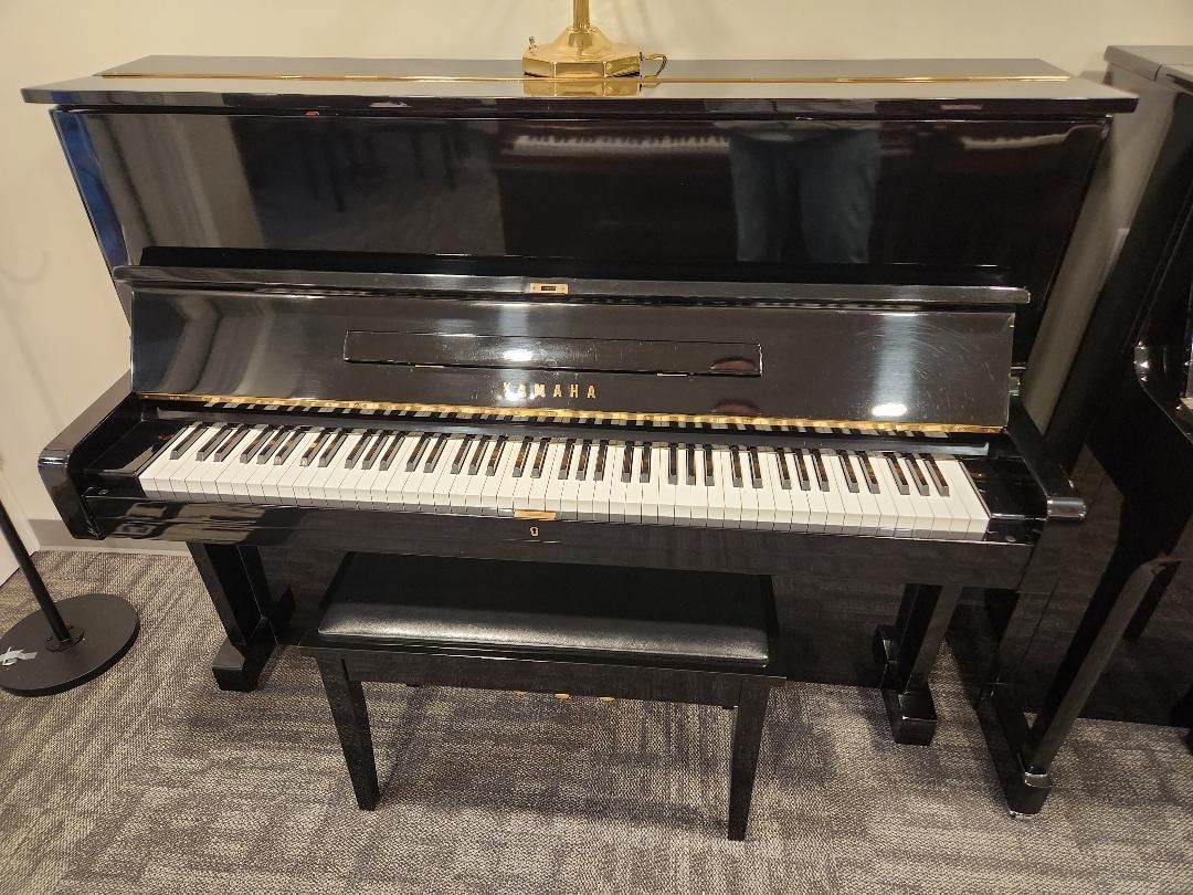 A black upright piano with a matching bench, positioned in a room with a grey carpet floor.