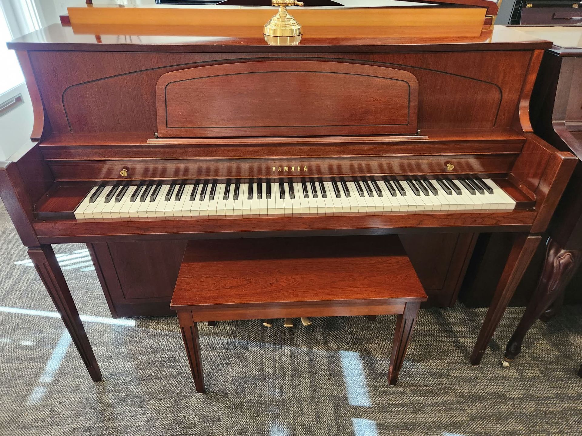Wooden upright piano with matching bench in a carpeted room
