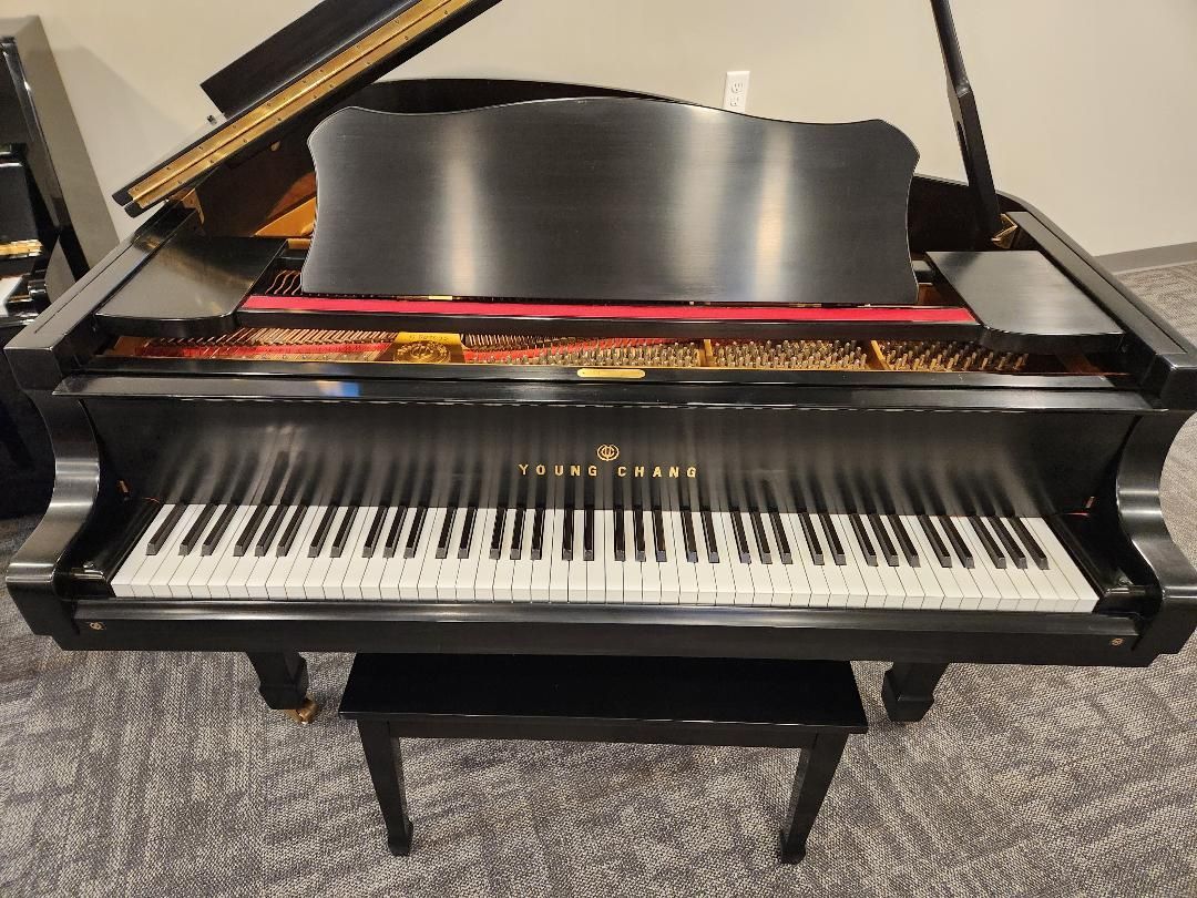 Black grand piano with open lid, keys visible, and bench in front.