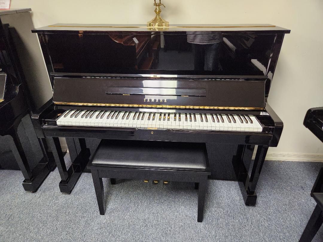 Black upright piano with bench; keys and music stand visible.