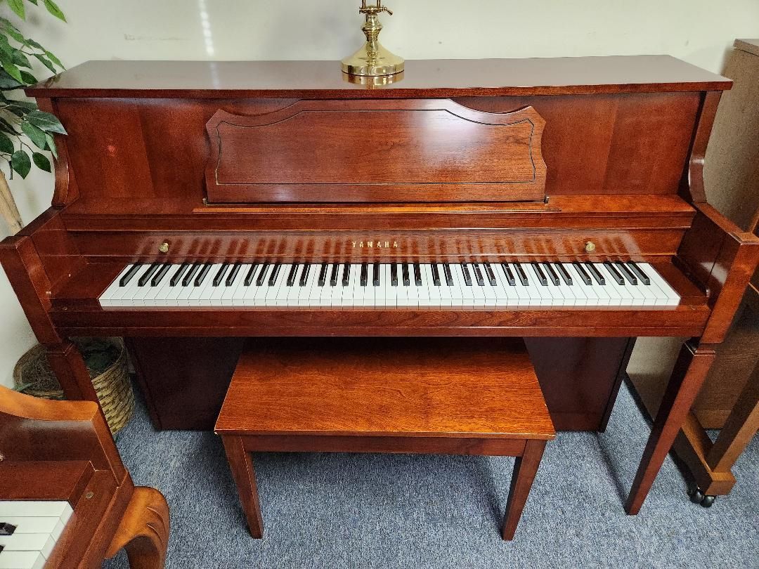 Brown upright piano with bench; gold lamp on top, keys blurred.
