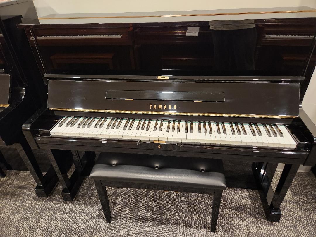 Black Yamaha upright piano with bench; glossy finish, keyboard visible.