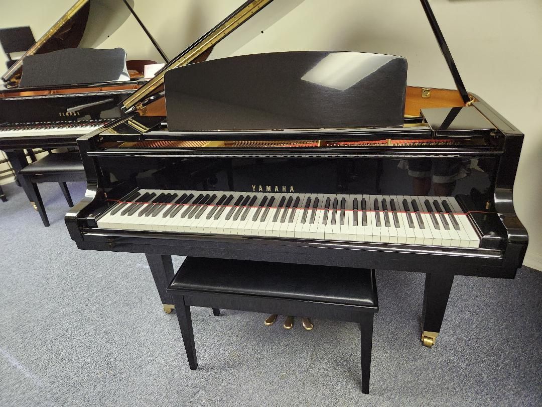 A black grand piano sits in a room with other pianos