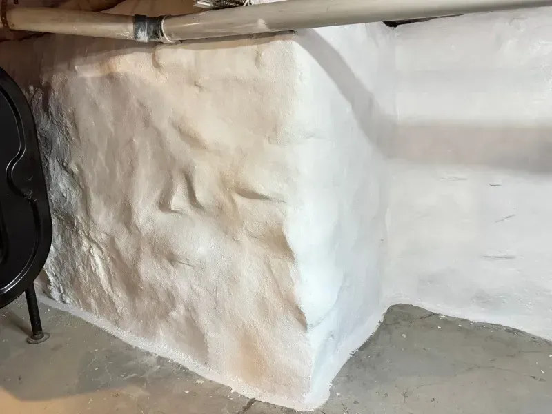 Whitewashed stone wall with a rough plaster patch and a gray concrete floor beneath a wooden beam.
