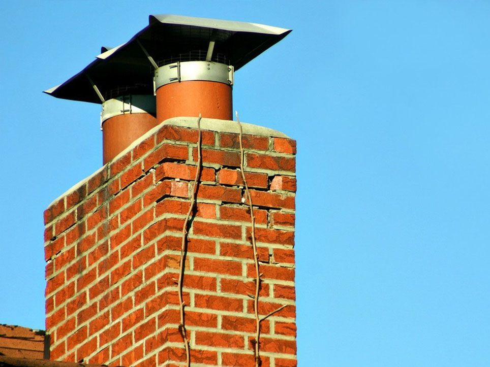 Brick chimney with two metal flues against a blue sky