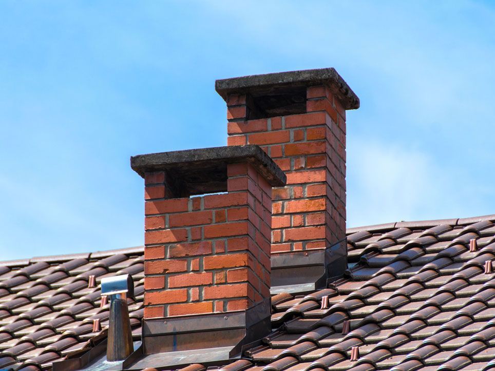 Two brick chimney stacks on a tiled roof under a blue sky