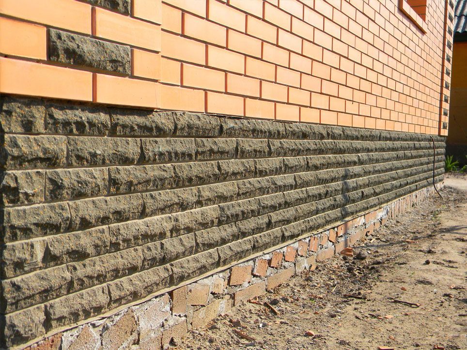 Brick building with a dark stone foundation and exposed dirt ground along the side.