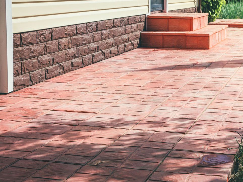 Brick patio beside a house with stone retaining wall and steps in warm sunlight