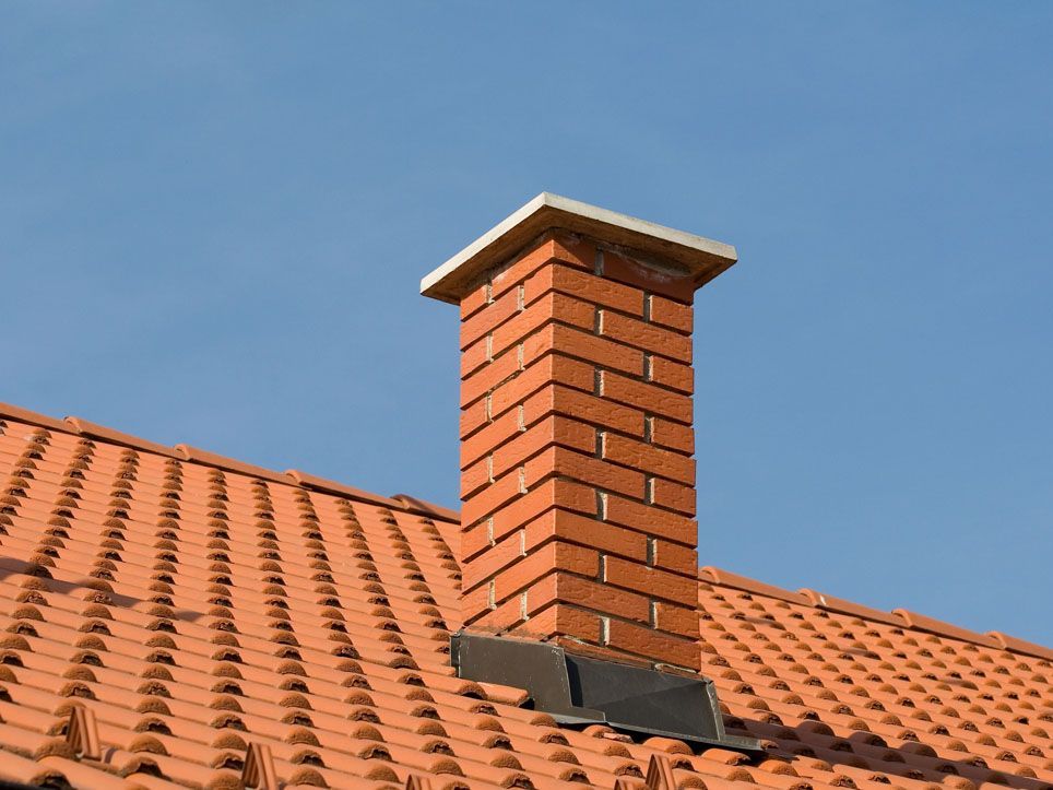 Red brick chimney on a terracotta tile roof against a blue sky