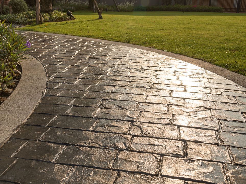 Curved wet stone walkway glistening in sunlight beside a green lawn and garden beds