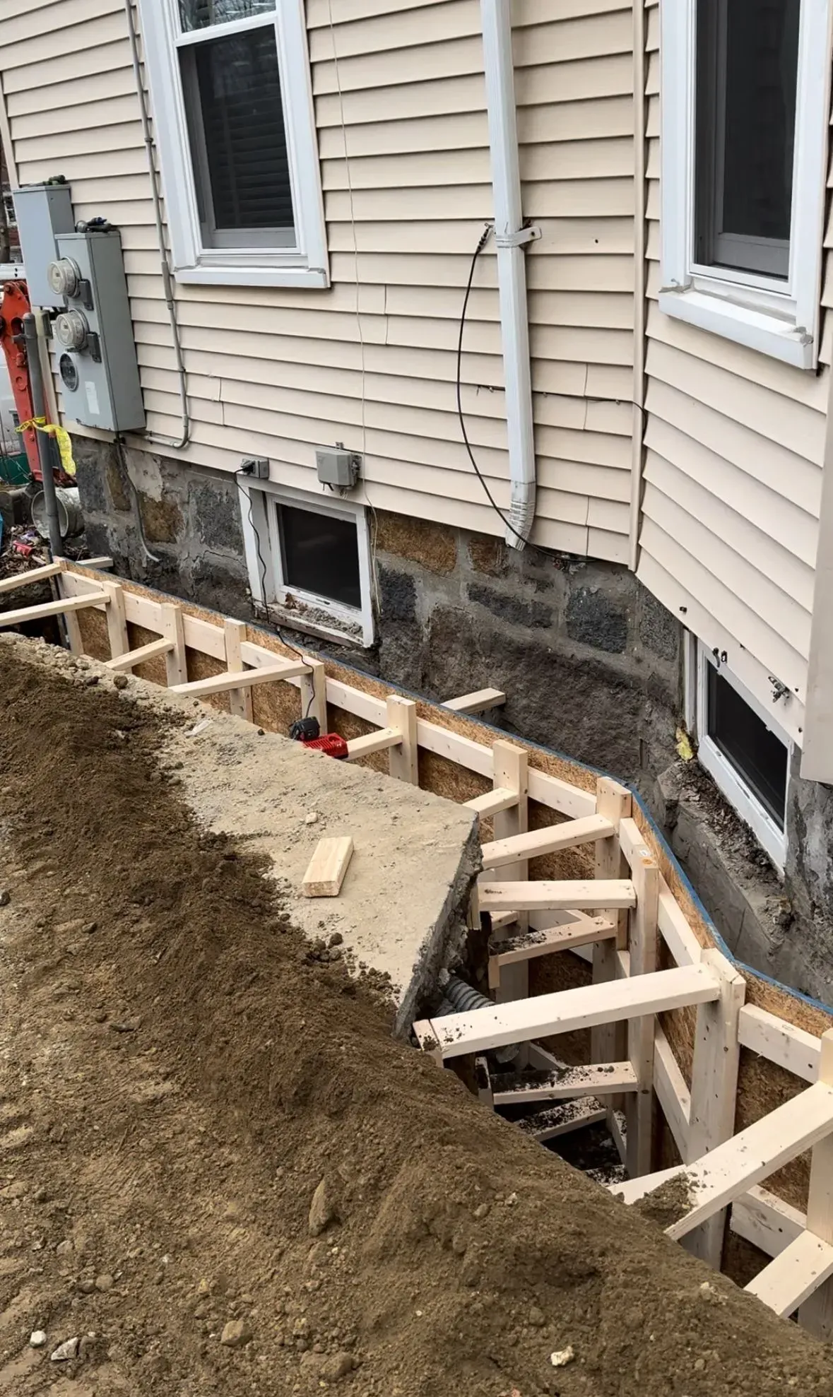 Wooden frame construction against a house foundation for a retaining wall. Earth mound in the foreground.