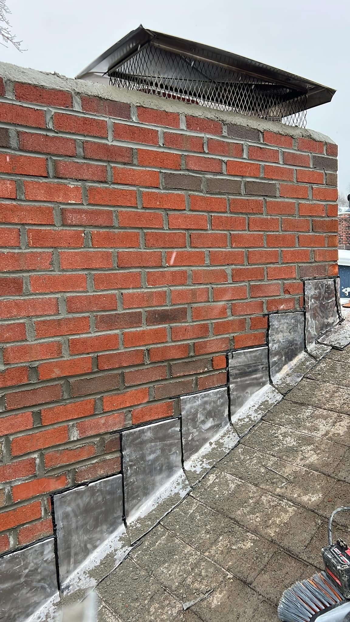Brick chimney with dark metal cap and flashing on a gray roof.