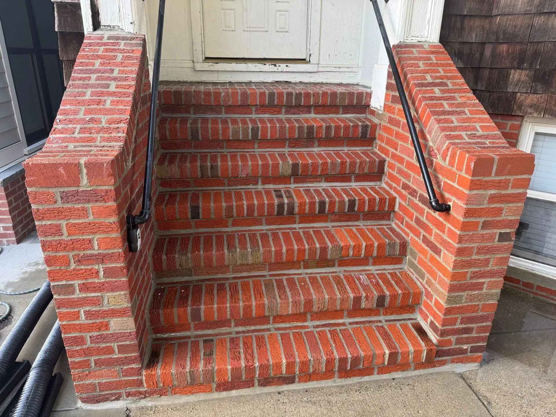 Brick steps leading up to a white door, with black handrails and brick side walls.