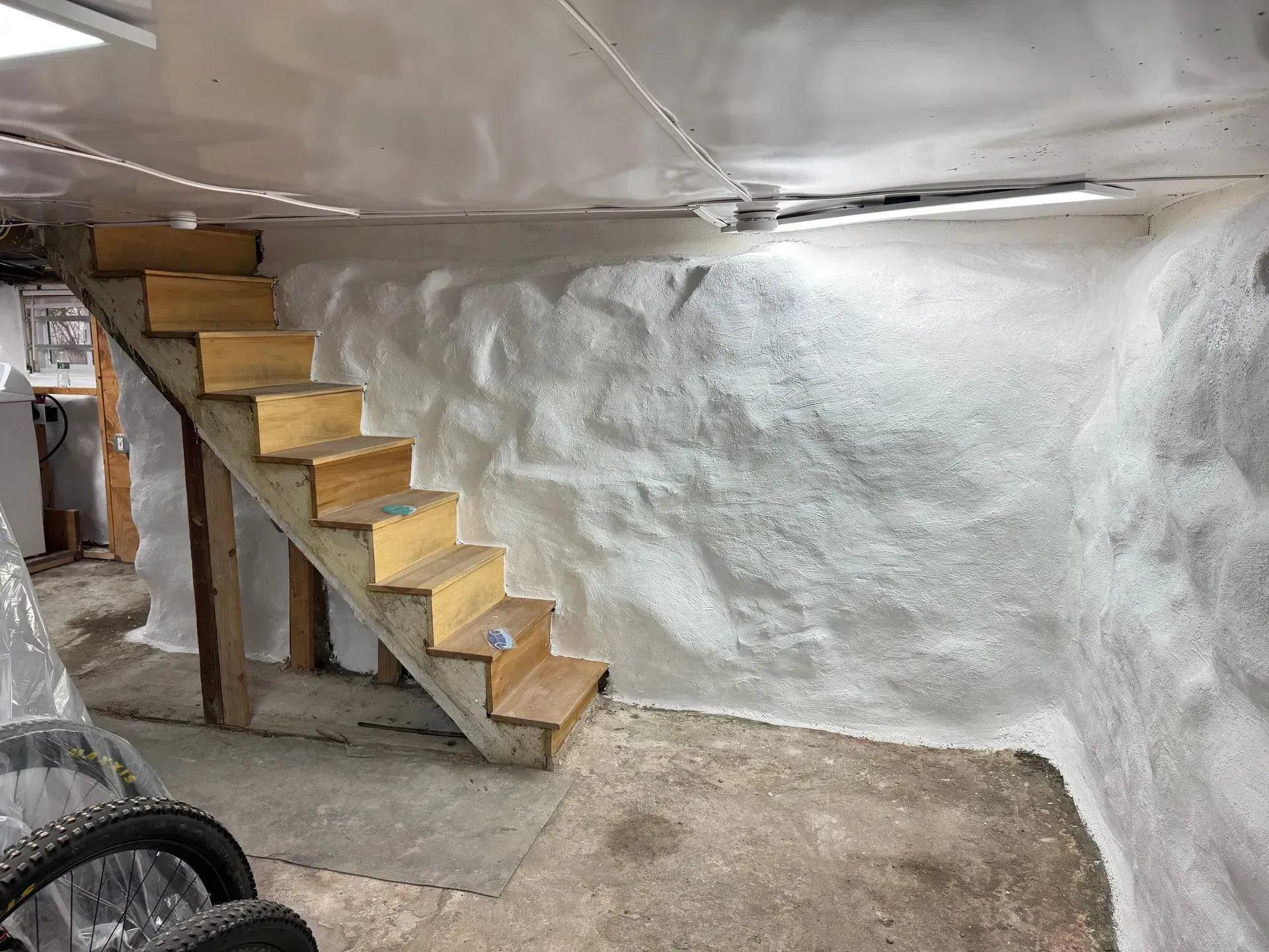 Wooden stairs against a textured white wall in a basement, with a concrete floor.