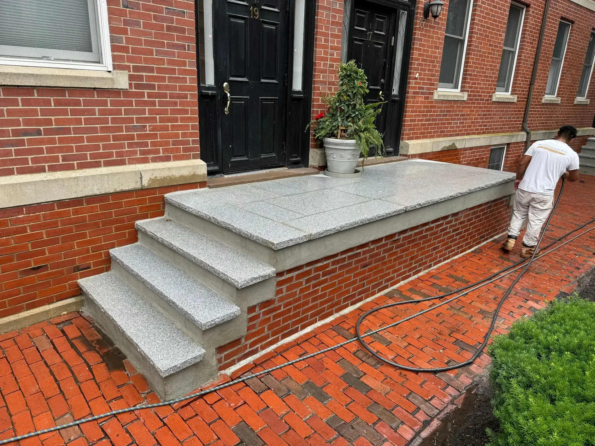 Brick building exterior with gray steps and a person washing the pavement.