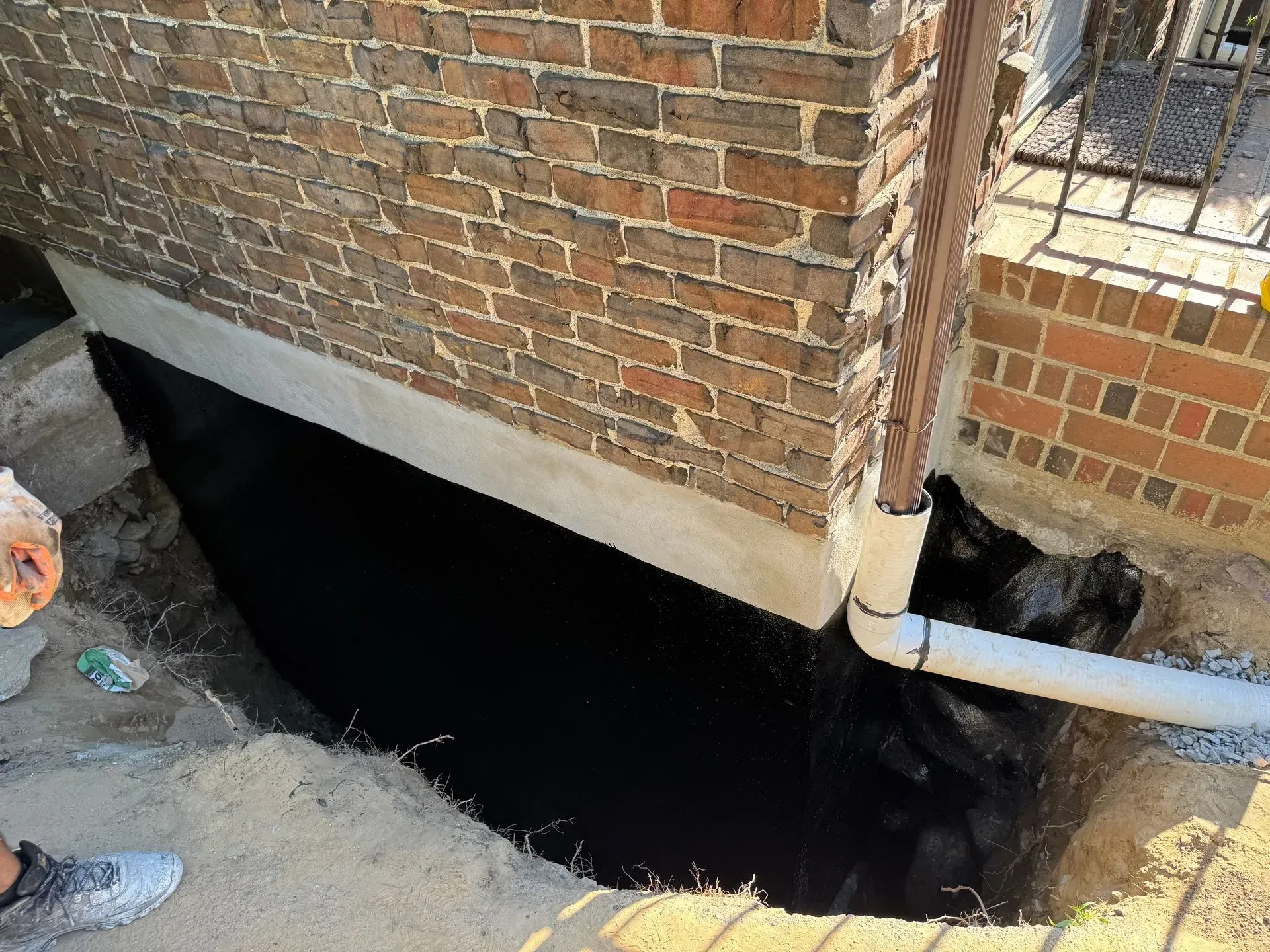 Black waterproofing membrane on a brick building foundation, exposed during excavation for drainage work.
