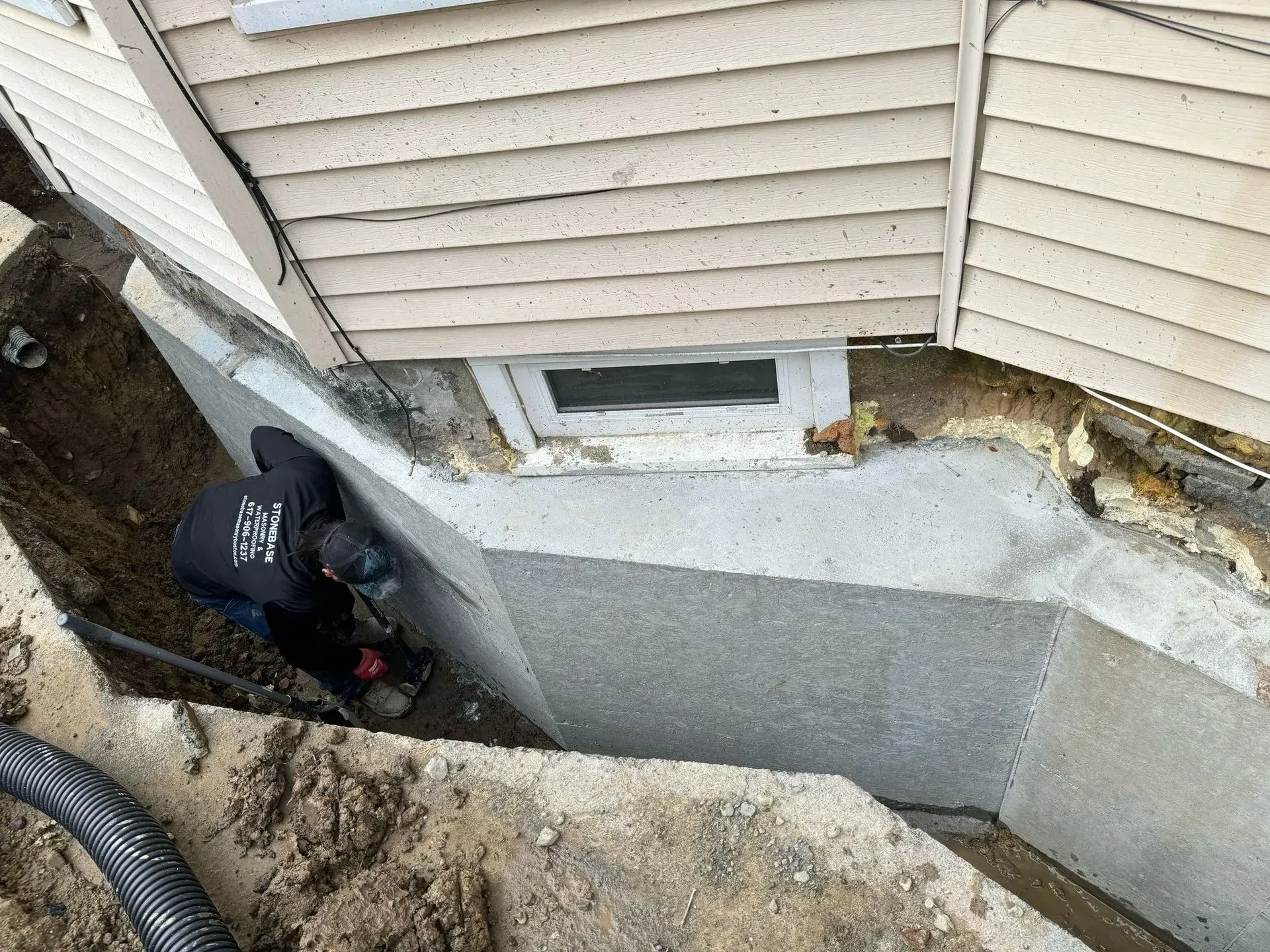 Person working on a concrete foundation next to a house with an excavated area.
