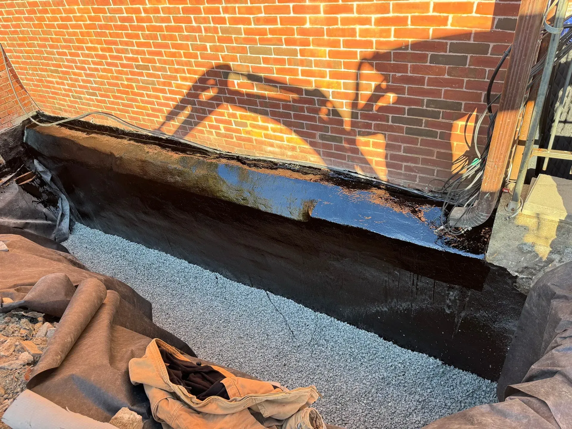 Foundation repair showing a brick wall with black waterproofing membrane and gravel.