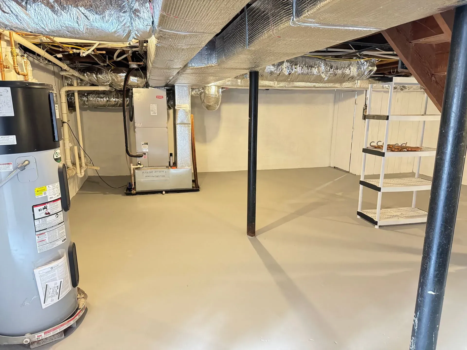 Basement interior with water heater, HVAC unit, support columns, and shelving unit. Light gray floor and white walls.