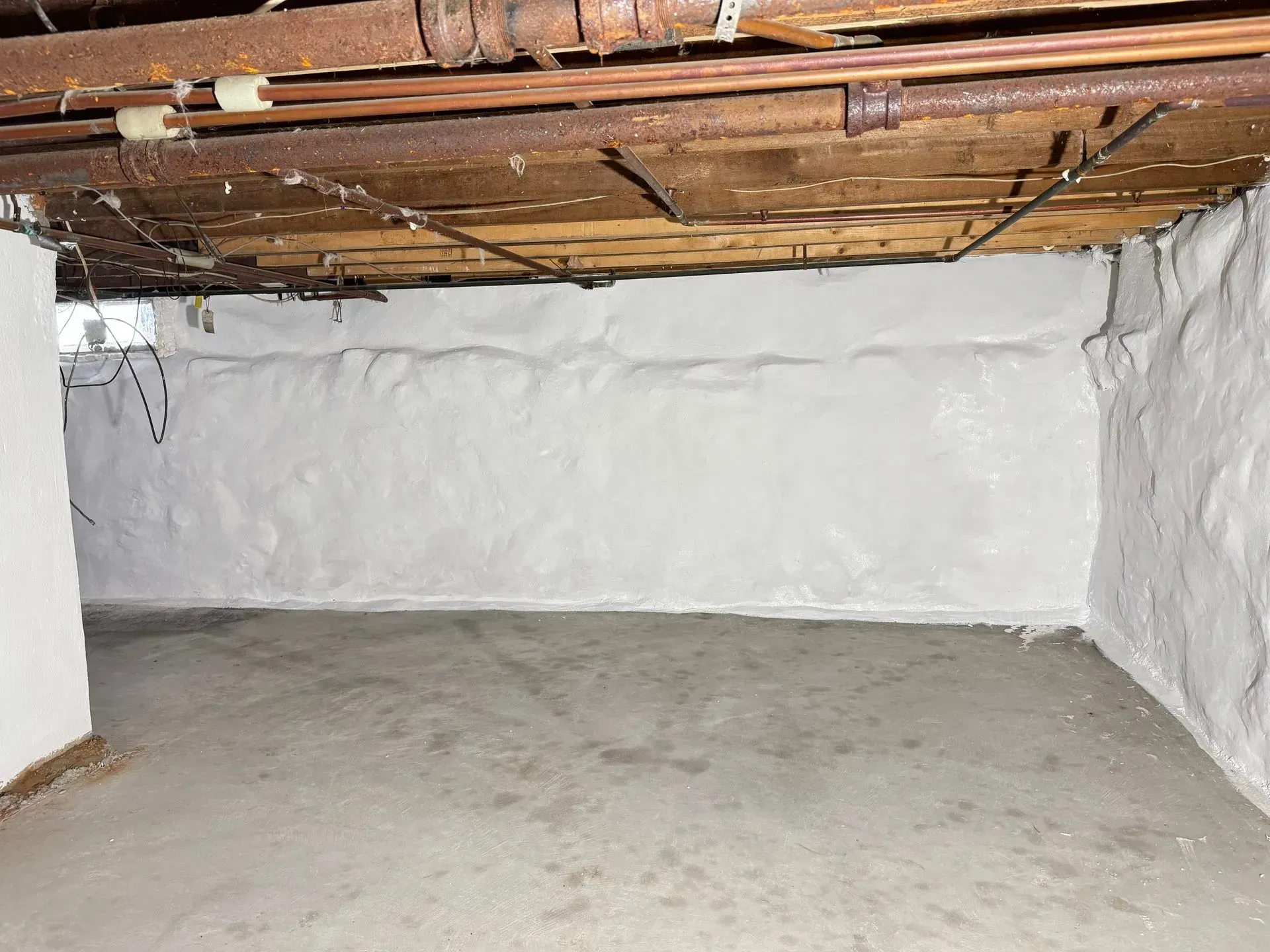 Basement with concrete floor, white painted walls, exposed pipes on the ceiling.