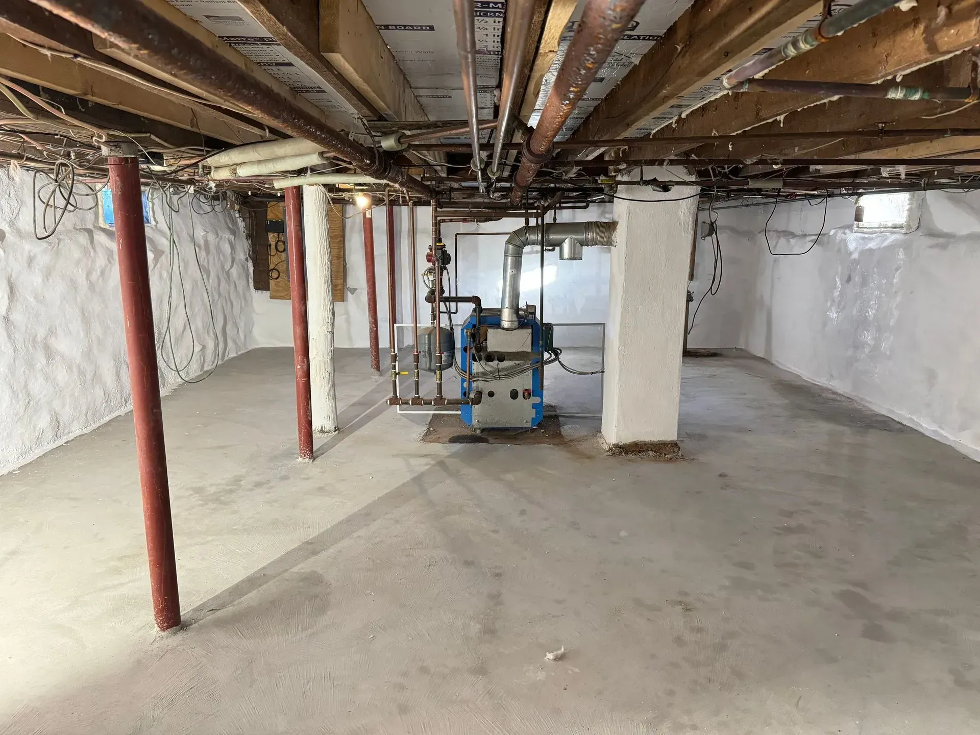 Basement with concrete floor, exposed pipes, support columns, and heating system.