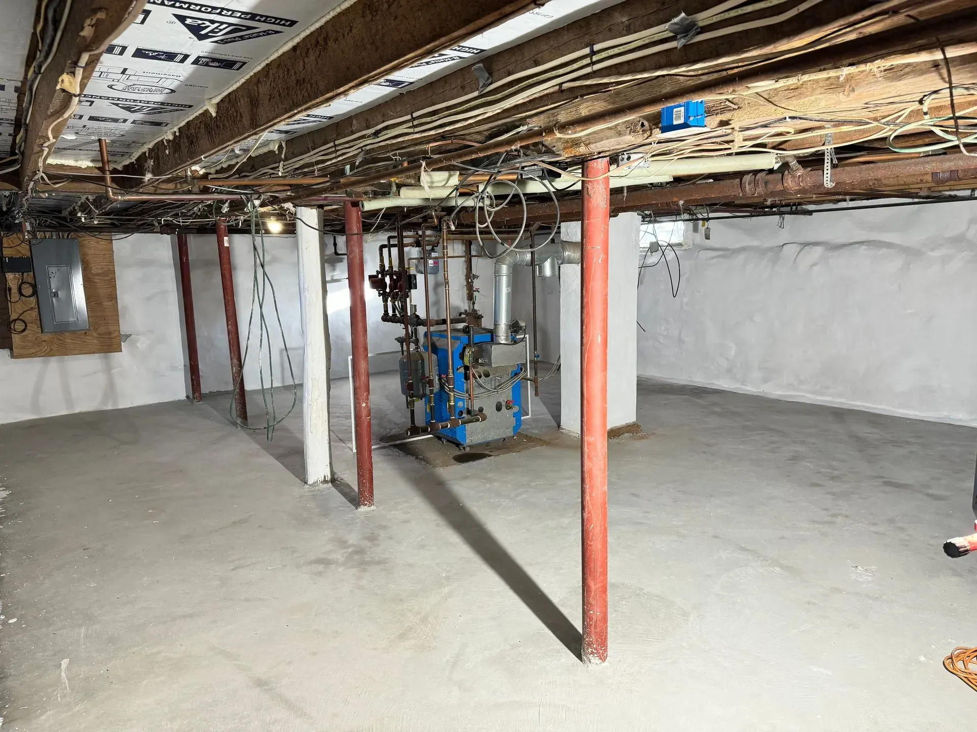 Basement interior with exposed beams, support columns, concrete floor, and central mechanical equipment.