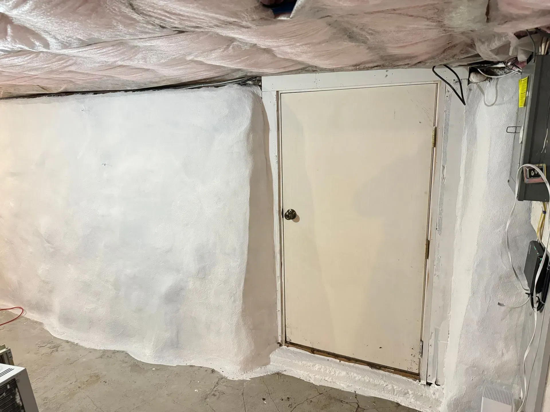 Basement storage area with white walls and a door. Exposed insulation on the ceiling.