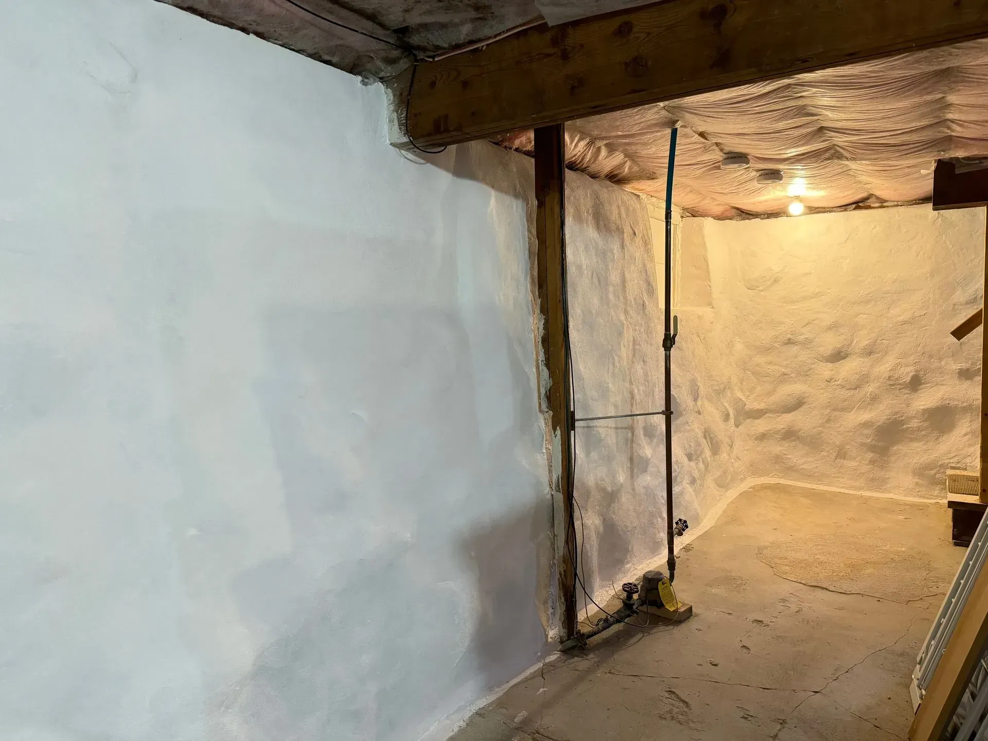 Basement interior with white-painted walls, exposed beam, pipe, and dim lighting.