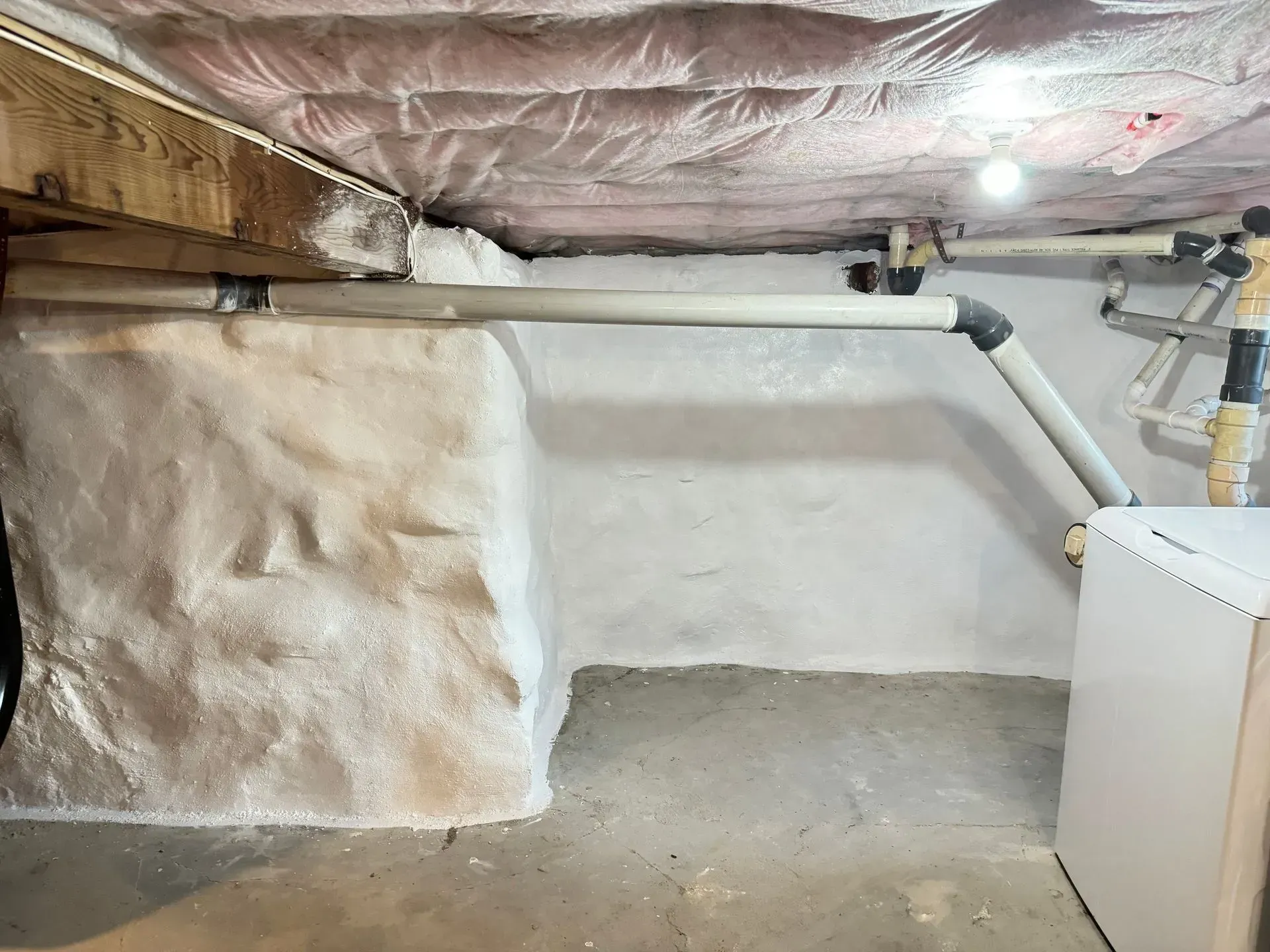 Basement interior with insulated ceiling, pipes, white walls, and a water heater.