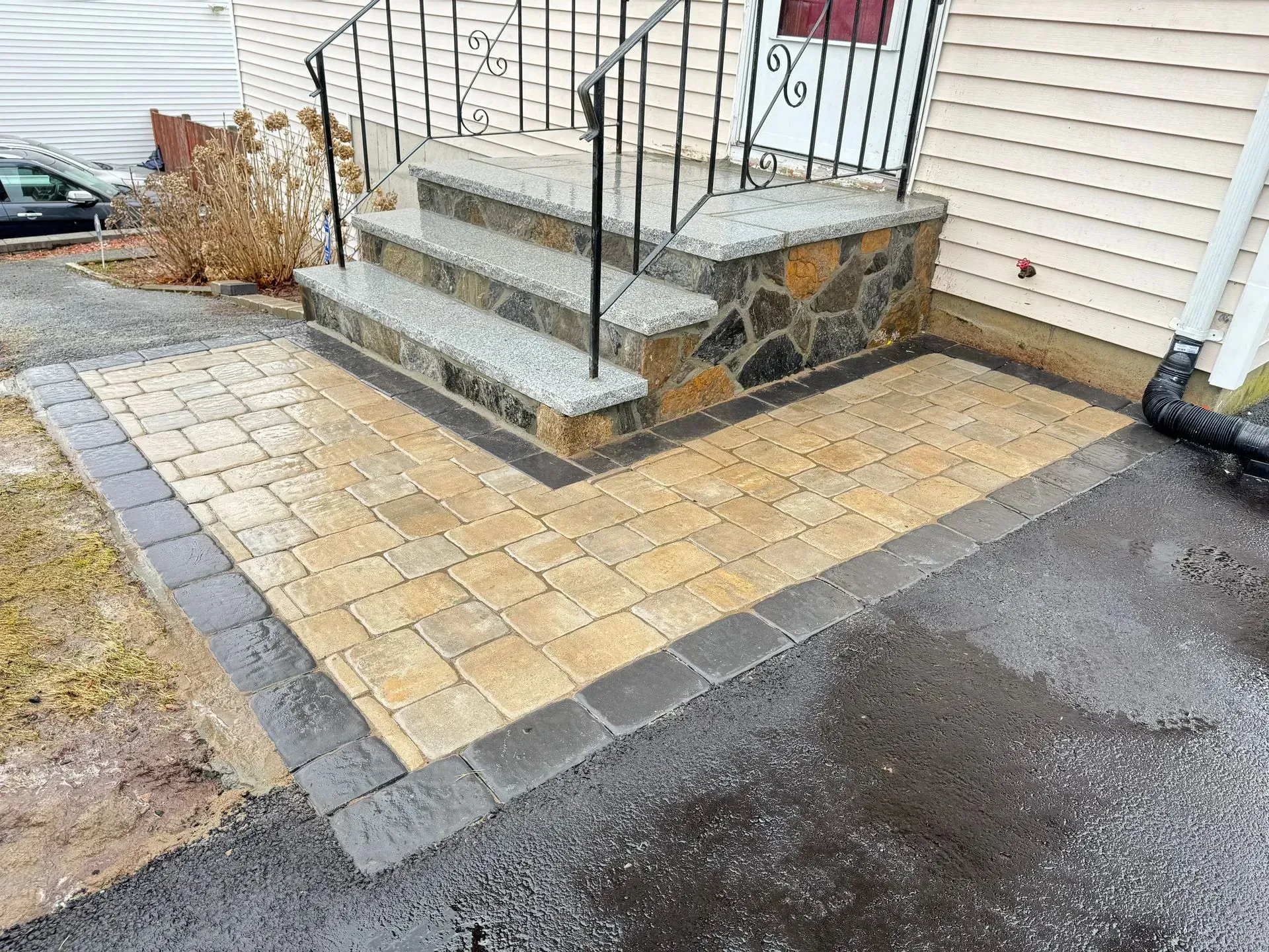 Brick pathway and steps leading to a house entrance. The steps have a stone veneer and a black railing.