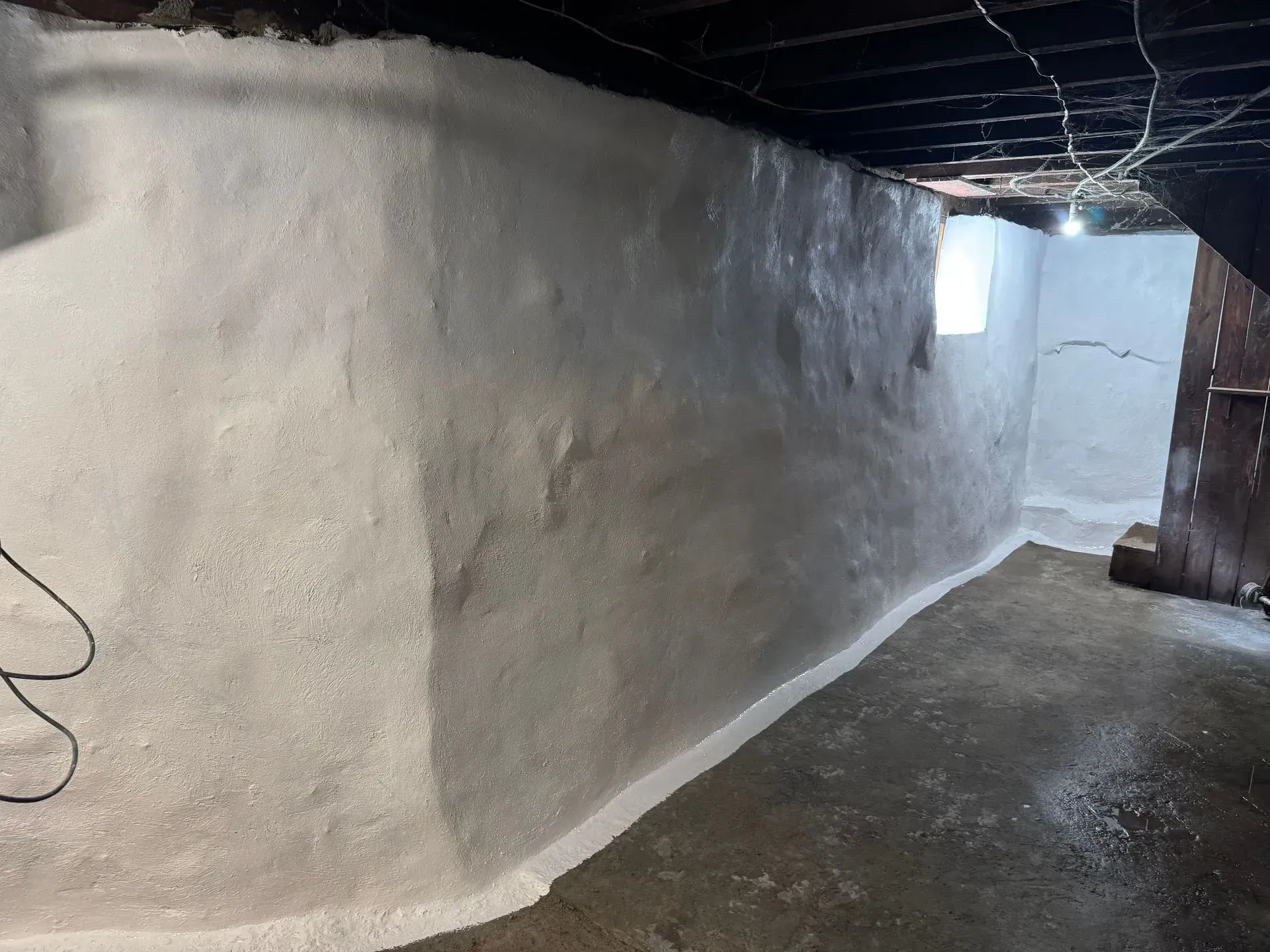 Basement wall with white coating, uneven surface, and concrete floor.