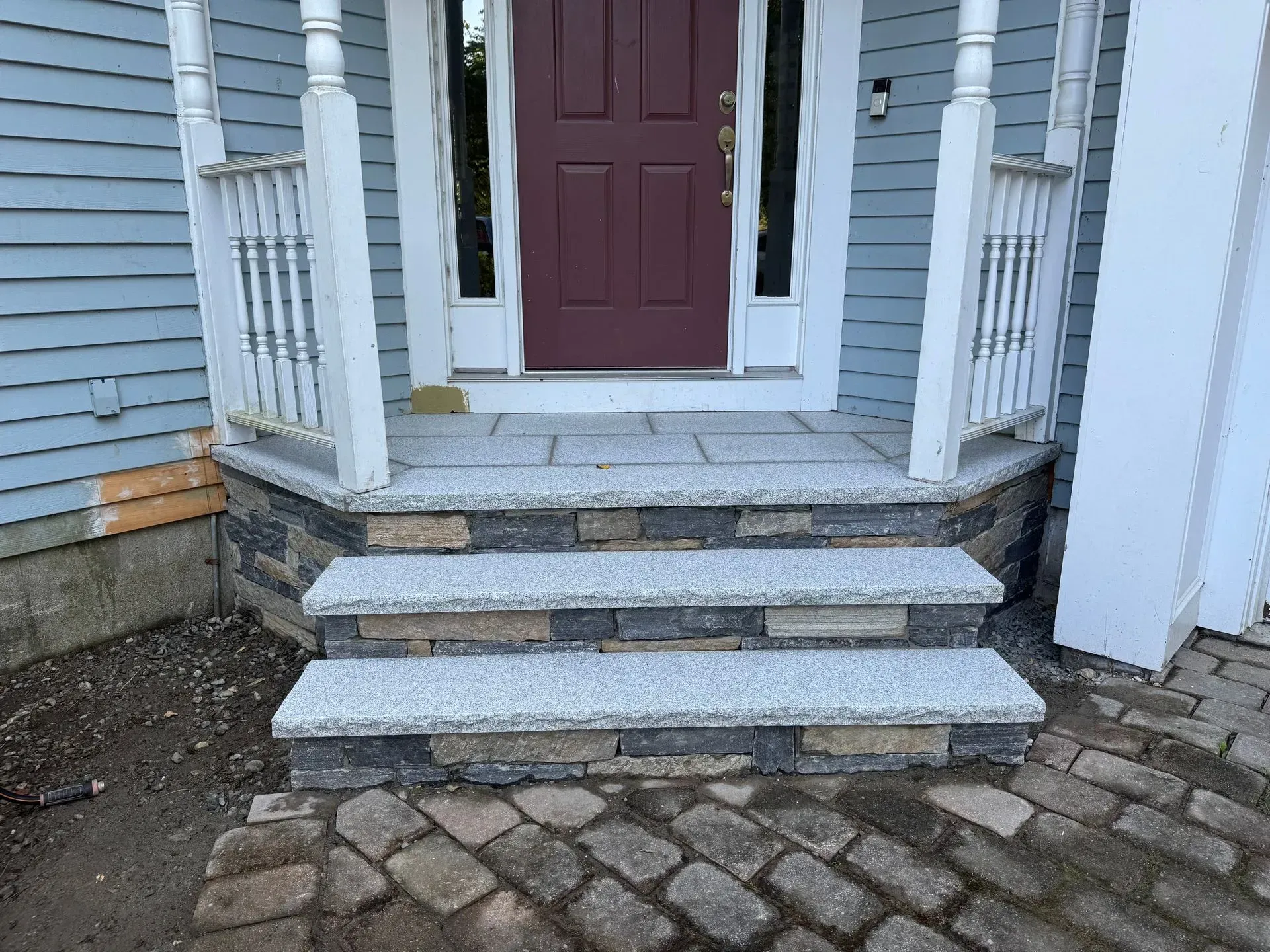 Stone steps leading to a front door with white porch columns, light blue siding.