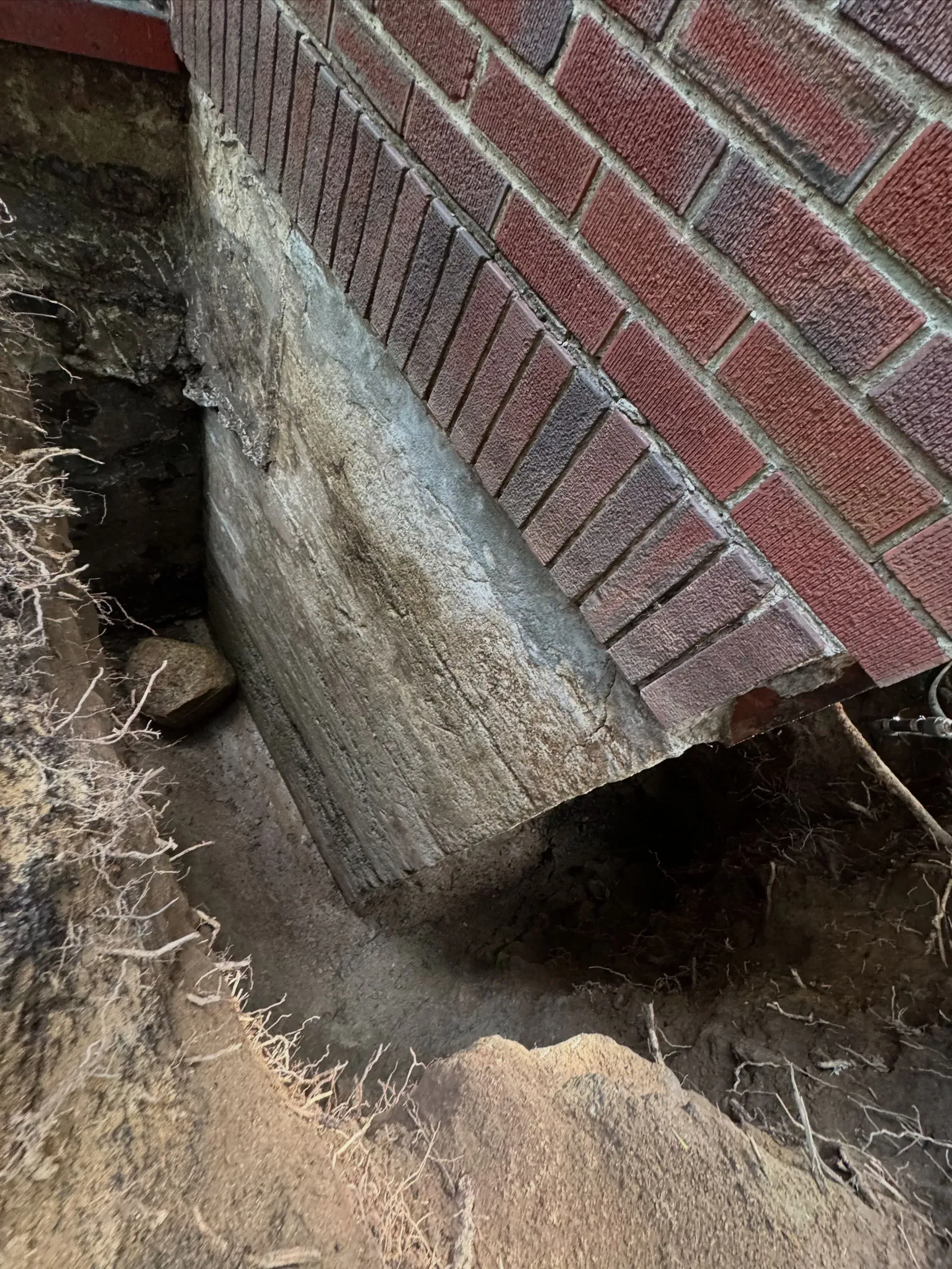 Excavated area next to brick foundation. Gray concrete block exposed with a section of red brick.