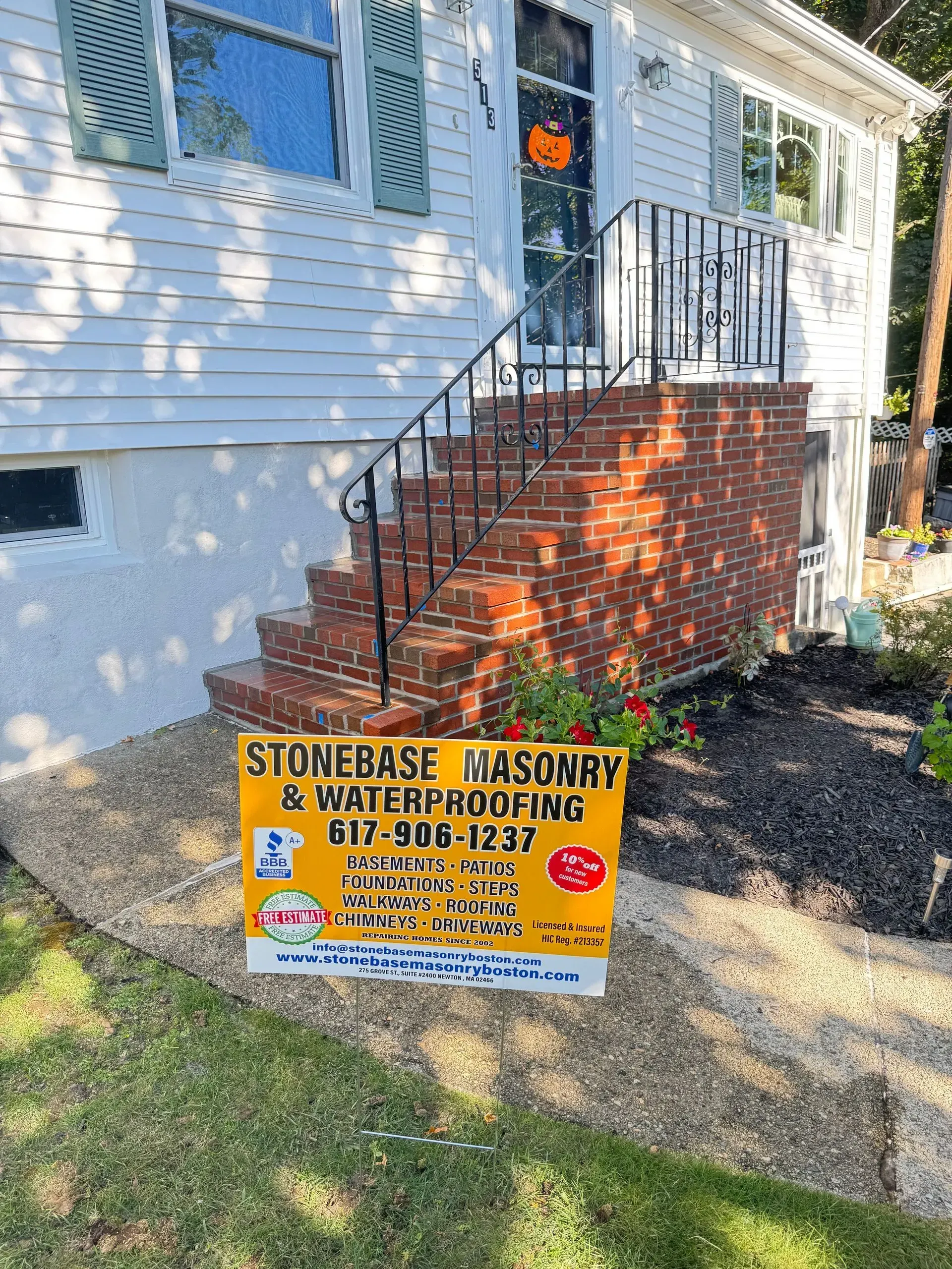 House with brick stairs, black railing, and Stonebase Masonry sign in front.