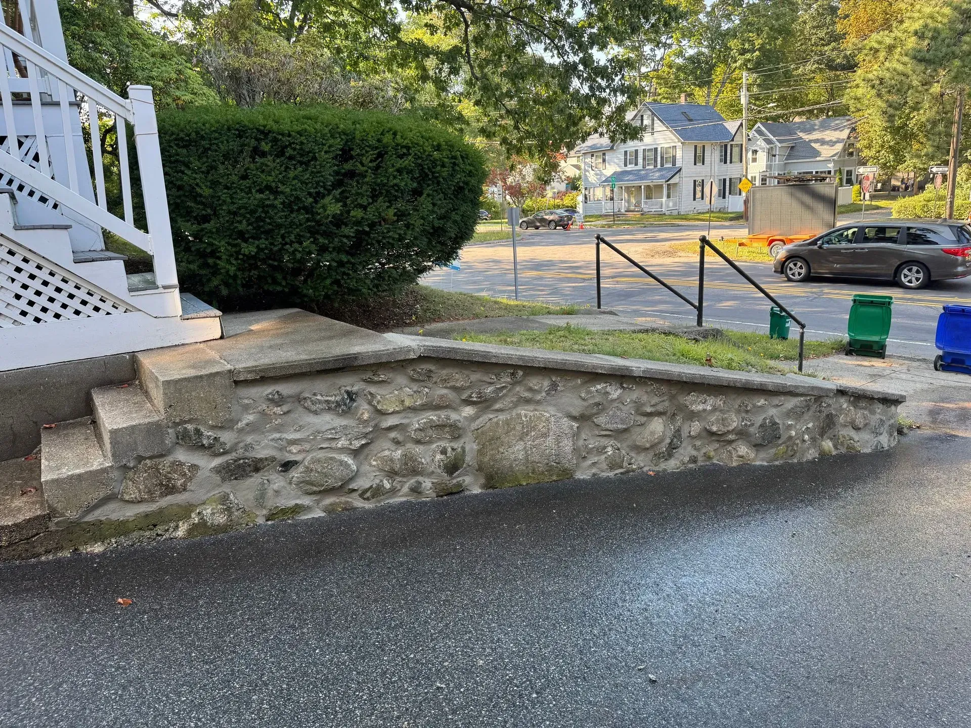 Stone retaining wall and steps leading to a house. Black railing and parked car in the background.