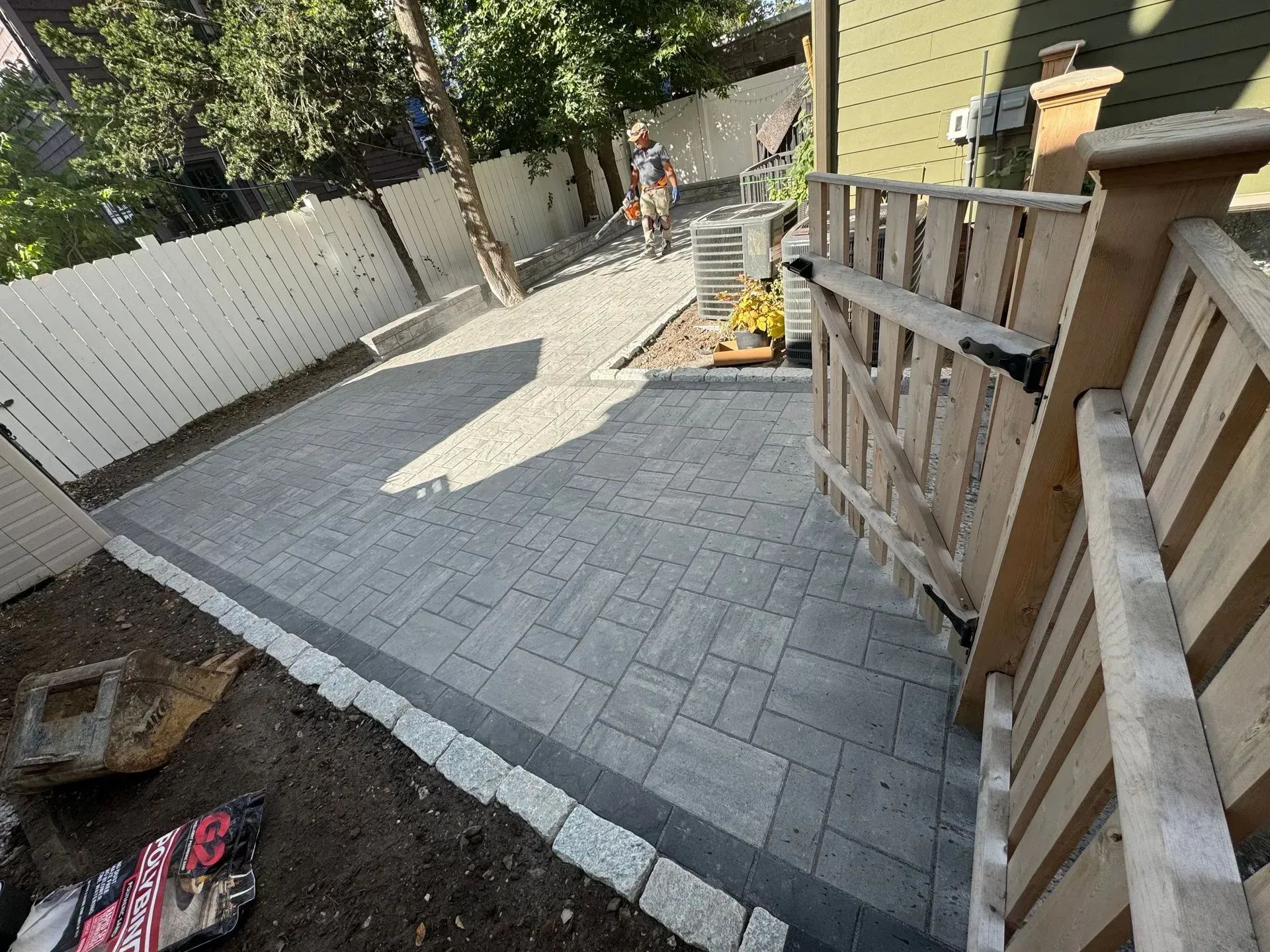 Gray paver driveway with bordering stones and wooden gate; person in background.