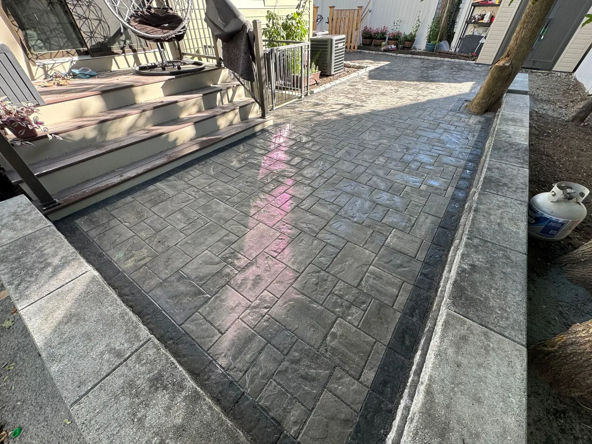 Brick patio with dark gray pavers, bordered by light gray blocks and a dark line, next to steps.