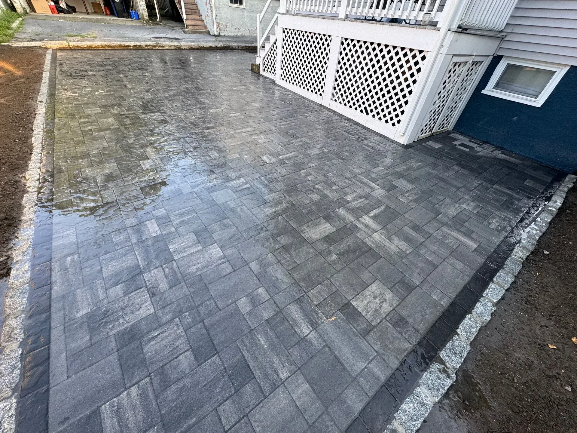 Newly installed gray paver patio next to a white deck with a dark blue house exterior.