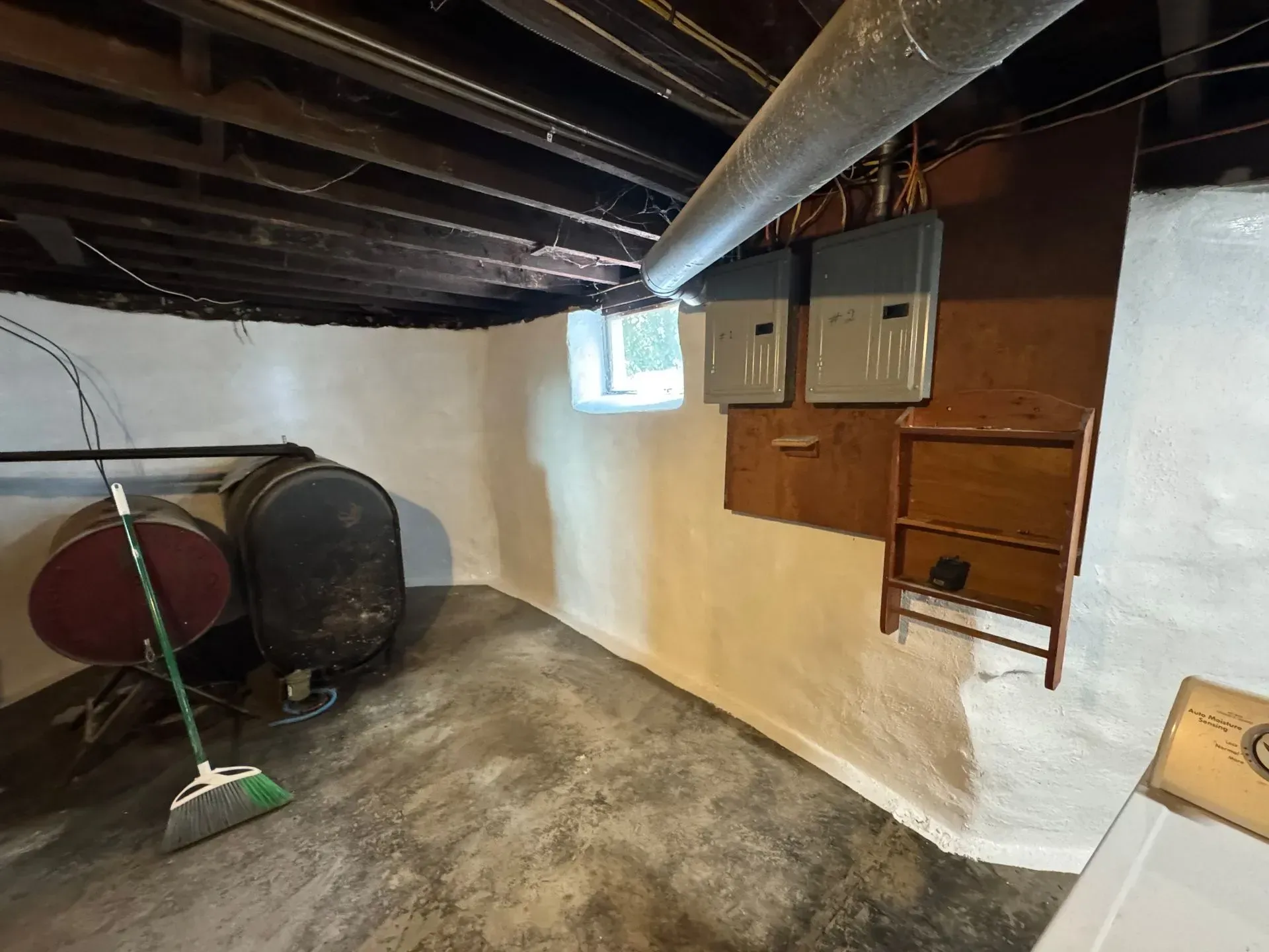 Basement interior with oil tanks, electrical panel, and a small window.
