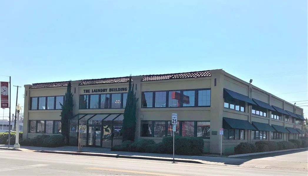 Two-story brick building with multiple windows, awnings, and landscaping under a clear sky.