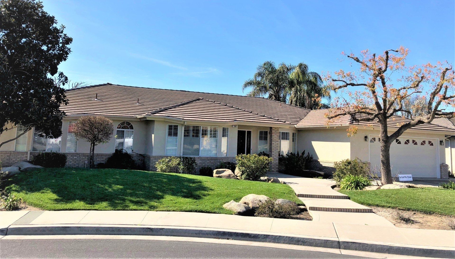Single-story home with a light-colored exterior, green lawn, and blue sky.