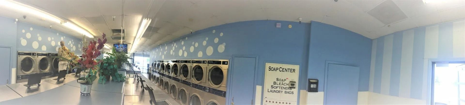 Interior of a laundromat with rows of washers and dryers. Blue and white walls, with decorative elements.