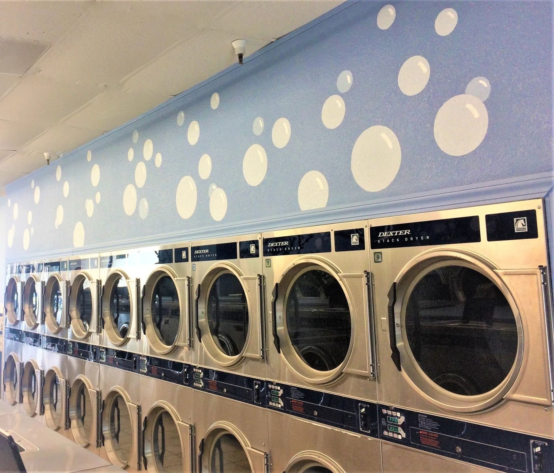 Row of washing machines in a laundromat, with blue wall painted with white bubbles above.
