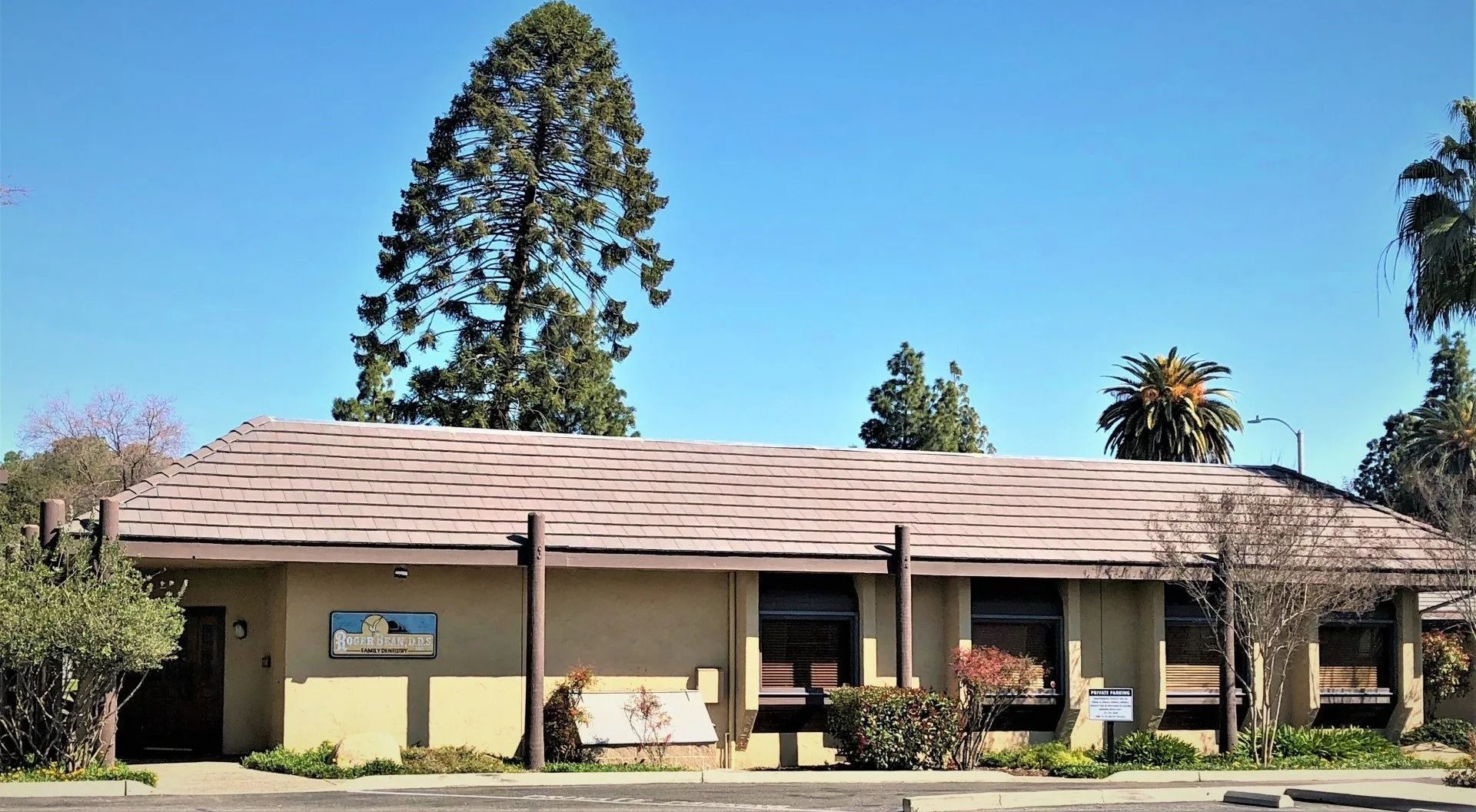 Tan building with tiled roof; tall tree behind. Sunny day.